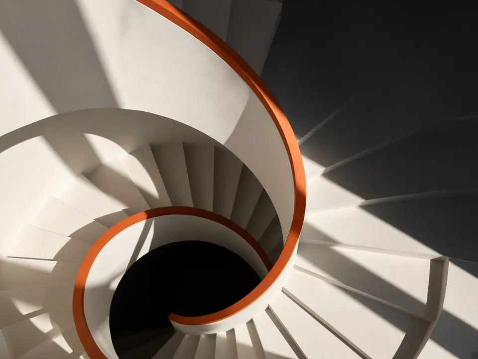 Photograph of a cream spiral staircase from above with an orange handrail